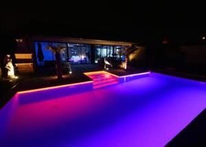 basen z fioletowymi światłami w ogrodzie w nocy w obiekcie Love room borabora 2 w mieście Trévoux
