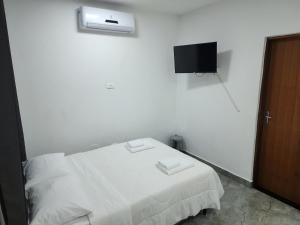 a bedroom with a white bed with a tv on the wall at Maresias Suítes in Maresias