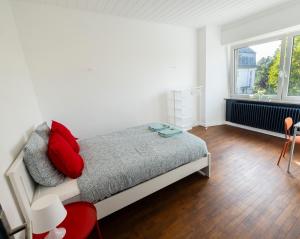 a bedroom with a bed with red pillows and a window at Tram station rooms by CityPillow since 2019 in Hesperange