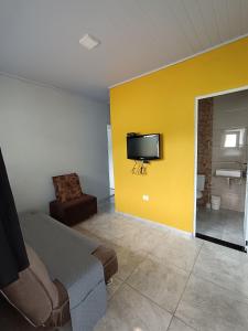 a room with a yellow wall with a bed and a television at Casa de Praia in Ubatuba