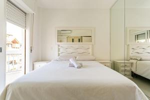 ein weißes Bett in einem weißen Schlafzimmer mit einem Spiegel in der Unterkunft Apto c/ sacada no Open Shopping Jurerê IBI307 in Florianópolis