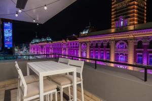 a white table and chairs in front of a building with purple lights at Found at Flinders - An Iconic City Stay in Melbourne
