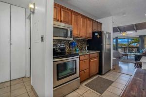 a kitchen with stainless steel appliances and wooden cabinets at Kihei Bay Surf 208- Updated partial oceanview studio across from beach in Kihei