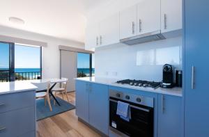 a kitchen with blue cabinets and a dining room with the ocean at Edgewater 1 - LJHooker Yamba in Yamba