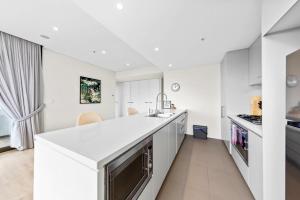 a white kitchen with a large white counter top at Amazing city view high level Apt in Sydney