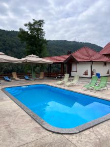 a swimming pool in front of a house with chairs and umbrellas at Grande Apartman Nature Connection Drina in Bajina Bašta