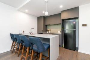 a kitchen with a counter with blue chairs and a refrigerator at Metropol 3 • Comfy• Luxury• Central • Free Parking in Canberra