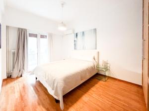 een witte slaapkamer met een bed en een houten vloer bij Harmonia ANhome Premium Selections in Athene