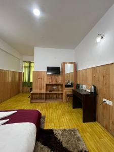 a room with a bed and a desk and a television at Hotel Tashi Ga Tsel in Tawang