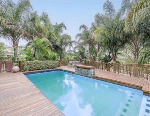 a swimming pool with a wooden deck and trees at Palms On Byrne: Where Elegance Meets Serenity in Durban