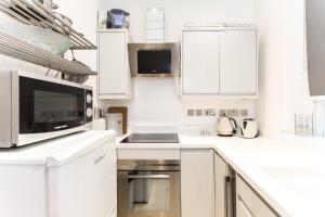 a white kitchen with white cabinets and a microwave at Bright Warwick Chambers Apartment in London