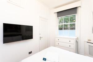 a white bedroom with a flat screen tv on a wall at Bright Warwick Chambers Apartment in London