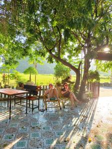 dos personas sentadas en un banco bajo un árbol en Tam Coc Sunshine Homestay, en Ninh Binh