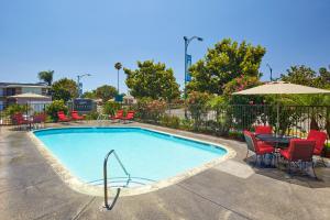 een zwembad met stoelen, een tafel en een parasol bij Eden Roc Inn & Suites near the Maingate in Anaheim