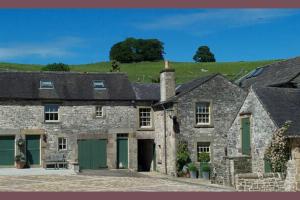 an old stone house with green doors and a grassy hill at Church Farm Holiday Cottages - Pinster Cottage in Ashbourne