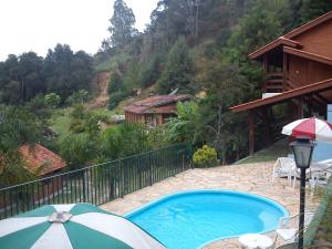 a swimming pool with an umbrella next to a house at Chalés Pousada Serra Negra in Serra Negra