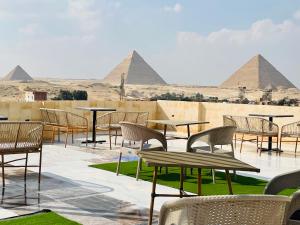 a patio with tables and chairs with pyramids in the background at Golden mask pyramids inn in Cairo