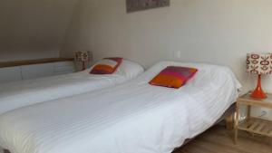 2 bedden in een kamer met witte lakens en kleurrijke kussens bij Maison récente à 300 m de la mer in Carantec