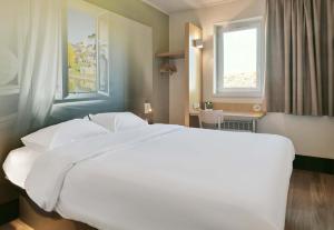 Cette chambre comprend un grand lit blanc et une fenêtre. dans l'établissement B&B HOTEL Le Mans Nord 1, à Saint-Saturnin