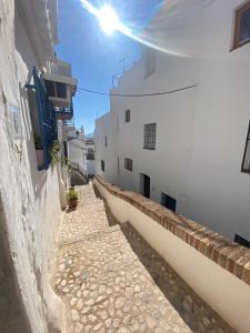 un callejón entre dos edificios blancos con el sol brillando en Casita del Tejedor, en Frigiliana