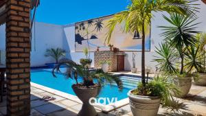 a pool with palm trees in pots next to a building at Qavi - Casa Tropical #ParaísoDoBrasil in Touros