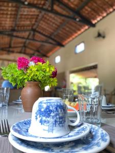 a table with a cup and plates and a vase with flowers at Aldeia Patacho in Pôrto de Pedras