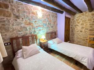 2 camas en una habitación con una pared de piedra en Mas de Nofre, en Peñarroya de Tastavins