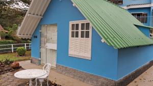 a blue house with a green roof and a table and chair at Meu Chalé in Miguel Pereira