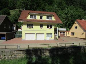 a yellow house with white garage doors next to a river at FeWo Harz Haennig 2 in Walkenried