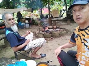zwei Männer auf einem Stuhl vor einem Feuer in der Unterkunft CAMPSITE CMM YAN KEDAH in Yan