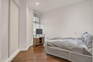 a white bedroom with a bed and a television at Heathrow 2-Bedroom Urban Oasis in London