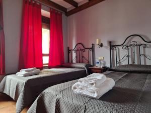 2 Betten in einem Zimmer mit roten Vorhängen und Handtüchern in der Unterkunft Hostal La Plata in Oropesa