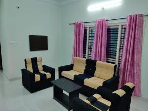 two chairs and a couch in a room with pink curtains at Galaxy Villa's Homestay 8431o31389 in Mysore