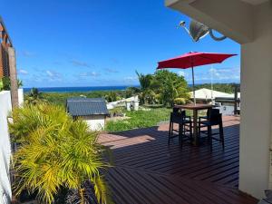 eine Holzterrasse mit einem Tisch und einem Sonnenschirm in der Unterkunft Villa 3 grandes chambres . in Sainte-Anne