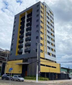 un gran edificio amarillo y gris con coches aparcados delante en Apto central e próximo à praia, en Torres