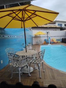 a table and chairs with an umbrella next to a swimming pool at suites com piscina praia dos anjos in Arraial do Cabo