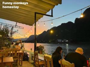 a group of people sitting at a restaurant near the water at Funny Monkeys Homestay in Phong Nha