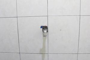 een klep op een witte betegelde muur in een badkamer bij OYO Life 93157 Kos Kaloka in Tanjung