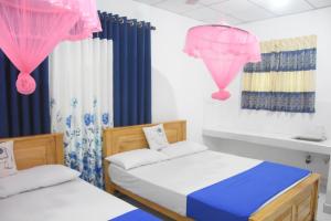 two beds in a room with pink and blue curtains at Lion Home Stay Anuradhapura in Anuradhapura