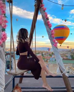 a woman sitting on a swing with a hot air balloon at View Cave Hotel in Goreme