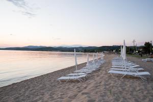 a row of white chairs and umbrellas on a beach at Eco Green Living in Toroni