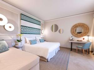 ヴィッラシミーウスにあるPullman Almar Timi Ama Resort & Spaのベッド2台とデスクが備わるホテルルームです。