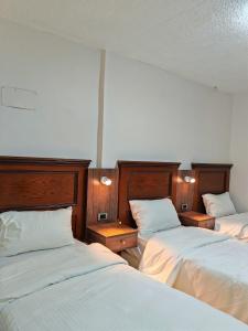 three beds in a room with white sheets at Cleopetra Hotel in Wadi Musa