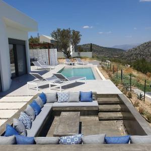 uma piscina com um sofá e almofadas em frente a uma casa em Nafplio Villa, pool & sea view em Tolo