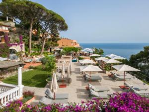 a patio with chairs and umbrellas and the ocean at Hotel Punta Tragara in Capri