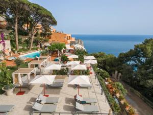 eine Reihe von weißen Sonnenschirmen und Stühlen neben einem Pool in der Unterkunft Hotel Punta Tragara in Capri