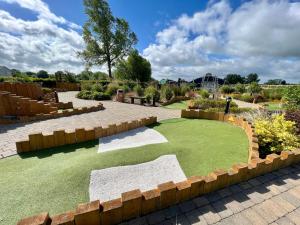 a garden with grass and a retaining wall at Puddleducks, Dog Friendly Hot Tub Lodge in South Cerney
