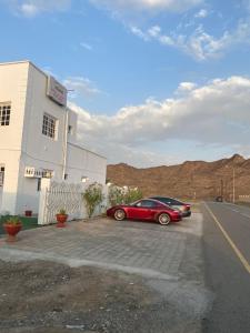 un'auto rossa parcheggiata in un parcheggio accanto a un edificio di Tafadal a Ibrā
