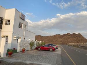 un'auto rossa parcheggiata accanto a un edificio sul lato di una strada di Tafadal a Ibrā