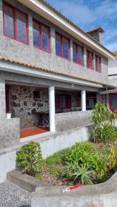 een stenen huis met rode ramen en een veranda bij SERRADO Da EIRA in Lajes das Flores